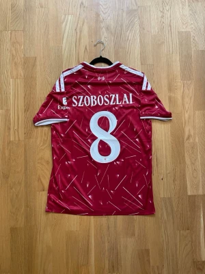 Szoboszlai #8 - M - Säljer en röd Liverpool matchtröja med Szoboszlai och nummer 8 på ryggen. Tröjan har vita detaljer, klubbmärke och Adidas-logga på bröstet samt sponsortryck. Tillverkad i lätt och ventilerande material, perfekt för fotboll eller träning.