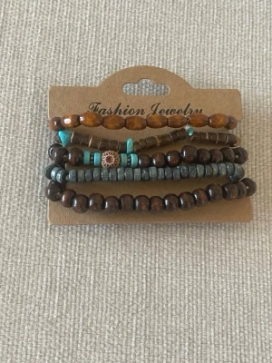 Set med pärlarmband i trä och turkos - Säljer ett set med fyra pärlarmband i olika färger och former. Armbanden har bruna, grå och turkosa pärlor i trä och plast, vissa med detaljer i guld. Perfekt för dig som gillar boho-stil och vill mixa flera armband tillsammans.