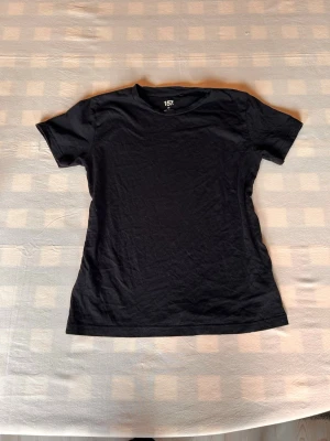Svart basic t-shirt - En enkel svart t-shirt med rund hals och korta ärmar. Perfekt basplagg som passar till allt och är gjord i mjukt bomullsmaterial. Snygg att styla med jeans eller kjol.