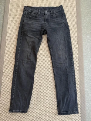 Levis 514 W30 L32 - Snygga svarta slim fit jeans från Levi's med klassisk femficksdesign och diskret slitning på låren. Jeansen har raka ben och en liten röd Levi's-tag på bakfickan. Perfekta för en avslappnad och trendig look. Väldigt bra skick 