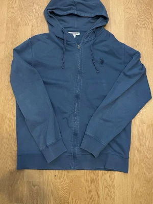 Polo Assn US Zip hoodie - Säljer en snygg och stilren U.S. Polo Assn. hoodie med dragkedja. Mörkblå/blågrå färg med broderad USPA-logga på bröstet. Perfekt till vardags, skolan eller en avslappnad outfit. • Full zip • Huva med dragsko • Broderad logga på bröstet • Bekväm och lätt att matcha • Bra använt skick  Storlek: M men passar jätte bra för S med.  Hör gärna av dig vid frågor eller bud! 