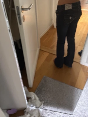 Mörkblå bootcut jeans - Säljer ett par mörkblå bootcut jeans med låg midja och klassiska fem fickor. Jeansen har kontrastsömmar och en patch bak i linningen. Perfekta för dig som gillar en retro och avslappnad stil.