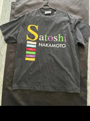 Satoshi Nakamoto t-shirt med tryck - Cool svart t-shirt med färgglatt Satoshi Nakamoto-tryck framtill och citat på ryggen. T-shirten har korta ärmar och normal passform. Materialet känns mjukt och skönt, perfekt för dig som gillar tech och krypto.
