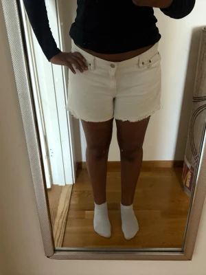 Vita jeansshorts med rå kant - Säljer ett par vita jeansshorts med rå kant nertill och klassisk femficksdesign. Shortsen har normal passform och midja, perfekta för sommaren. Snygga att matcha med en enkel topp eller hoodie.