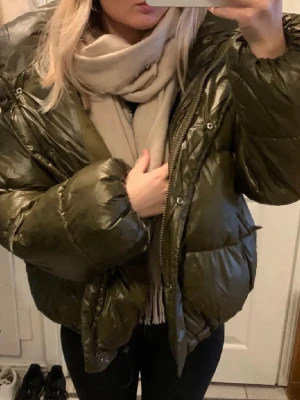Olivgrön glansig pufferjacka - Säljer en olivgrön pufferjacka med glansig finish och dragkedja framtill. Jackan har en stor huva och breda, vadderade partier som ger en riktigt puffig look. Endast använd fåtal gånger. Nypris: 800kr, säljer för endast 600kr!! (Första bilden ar lånad, den har inte knappar som bilden visar, annars identisk).