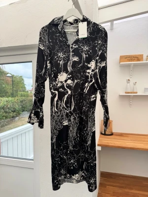 Svartvit långärmad skjortklänning - Stilren svartvit skjortklänning med krage och knappar framtill. Klänningen har ett unikt abstrakt mönster och långa ärmar. Perfekt för dig som vill ha en dressad look med edge. Ny med prislapp.