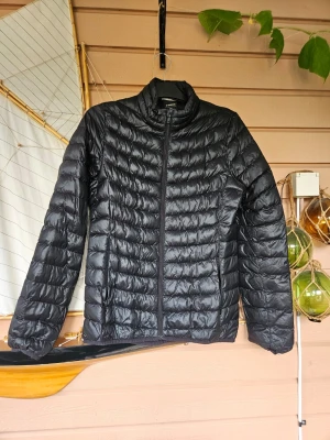 Svart lättviktsdunjacka - Snygg svart dunjacka med quiltat mönster och dragkedja framtill. Jackan har hög krage och två sidofickor. Perfekt för kyliga dagar och enkel att bära med sig tack vare den lätta designen.