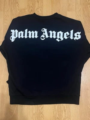 Palm Angels Tröja - Säljer en svart Palm Angels sweatshirt med den klassiska stora vita Palm Angels-loggan över ryggen.  Stilren oversized/streetwear-look som är lätt att matcha med jeans, cargos eller mjukisbyxor.  • Palm Angels • Crewneck • Bekväm passform • Använt skick – se bilderna  Storlek: M men skulle även passa perfekt till L.  Hör gärna av dig vid frågor eller bud! 