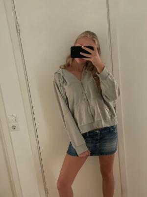 Ljusgrå zip hoodie med huva - Säljer en ljusgrå hoodie med dragkedja och huva. Hoodien har två stora fickor framtill och ribbade muddar vid ärmslut och nederkant. Perfekt för en avslappnad och chill stil.