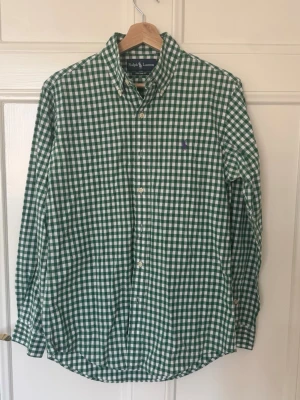 Grönvit rutig skjorta från Ralph Lauren - Snygg grön och vit rutig skjorta från Ralph Lauren i custom fit. Skjortan har klassisk krage, knappar framtill och lång ärm. Perfekt för dig som gillar en stilren och tidlös look.