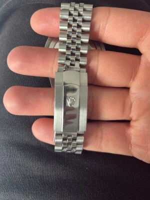 R Datejust jubilee - Stilren datejust klocka i silver med klassisk jubilee-länk och datumfönster. Urtavlan är också silverfärgad med tydliga indexmarkeringar och R-logga. Länken är i rostfritt stål och har en snygg, polerad finish. Perfekt accessoar för dig som gillar tidlös design.