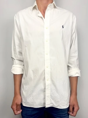 Polo Ralph Lauren Vit Skjorta Herr Storlek 16.5 - Klassisk vit skjorta från Polo Ralph Lauren i modellen Slim Fit med Easy Care Stretch. Tillverkad i 95% bomull och 5% elastan med broderad polo logga på bröstet. Skick B Grade. Storlek: 16 1/2 (ca 41 cm)  Mått [platt]: A: 47 cm B: 79 cm C: 63 cm D: 58 cm Tveka inte att höra av dig vid frågor eller funderingar. Skickas snabbt!