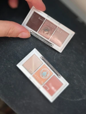 Depend  ögonskuggspalet - Säljer två små ögonskuggspaletter med tre nyanser vardera. Ena paletten har bruna och beige toner, den andra har varma nyanser i beige, orange och rosé. Båda har genomskinliga plastlock och kompakt format, perfekta att ta med i väskan.