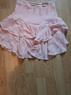Super söt somrig ljusrosa volangkjol 💗 - Söt ljusrosa kortkjol med volanger och omlottdetalj. Kjolen har bred smock i midjan för en bekväm passform och är gjord i ett lätt, luftigt tyg som passar perfekt till varmare dagar.💗 Inte super mycket använd 