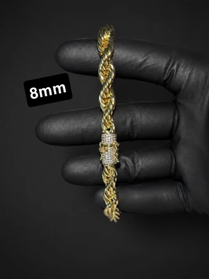 Guldpläterat cordell armband med diamantlås! - Säljer ett stilrent armband i guldfärgad metall med tvinnad kedjedesign, 8mm brett. Låset är dekorerat med små gnistrande stenar som ger extra bling. Perfekt för dig som vill ha ett statement-armband med exklusiv känsla.