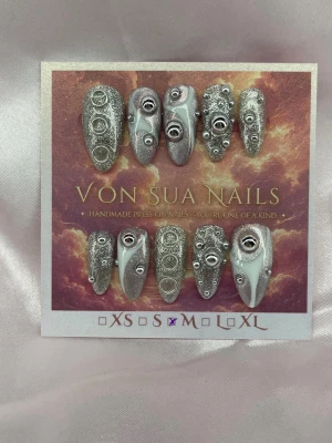 Rivet (M);Medium Almond - Handgjorda press-on nails i Medium Almond med silverglittrig bas, metalliska nitar, ringdetaljer och vita 3D-accenter. Varje nagel har sin egen design för ett futuristiskt, industriellt uttryck.  Storlek: M Form: Medium Almond 10 handgjorda naglar Prep-kit medföljer.