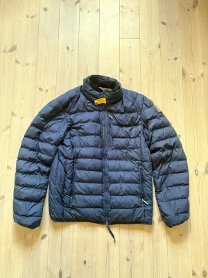 Mörkblå dunjacka från Parajumpers - Säljer en mörkblå dunjacka från Parajumpers i modellen Super Lightweight. Jackan har hög krage med gul tag. Trasig dragkedja. 
