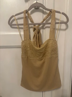 Ny Zara topp - Supersnygg beige linnetopp med pärlbroderier upptill och breda axelband som knyts i nacken. Toppen har en elegant omlottkänsla och tunna axelband för extra detalj. Perfekt för dig som vill sticka ut med en unik topp!