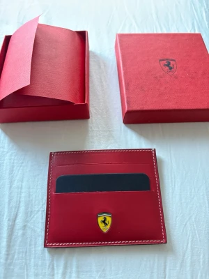 Röd Ferrari plånbok - Röd Ferrari plånbok. Plånboken är helt oanvänd men lådan är tyvärr lite smutsig.🤗Pros kan diskuteras 🤗 Nytt pris 2000:-
