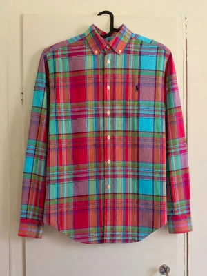 Polo Ralph Lauren rutig skjorta – M 10–12 år 🌈 - Superfin färgglad skjorta från Polo Ralph Lauren i klassiskt rutigt mönster. Kombination av rosa/rött, turkost, grönt och blått med den klassiska broderade Polo-loggan på bröstet. Button-down-krage och lång ärm. 👕 Storlek: M (10–12 år) 🧵 Material: 100 % bomull 🎨 Färg: flerfärgad/rutig ✨ Skick: Mycket bra utan defekter!😁 📏 Mått kan skickas vid intresse 📦 Skickas snabbt!