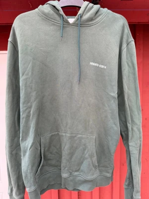 Grön hoodie från Axel Arigato - Snygg grön hoodie från Axel Arigato med trycket 'ARIGATO ©2014' på bröstet och ryggen. Hoodien har huva med dragsko, stor magficka och ribbade muddar. Perfekt för en avslappnad och trendig stil.
