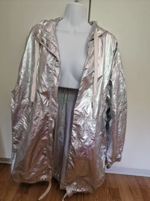 Silver metallic vindjacka med huva - Snygg silverfärgad vindjacka i metallic-look med huva och vita dragskor. Lite slitage vid ärmsluten, se sista bilden. 🤍