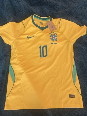 Gul Brasil Neymar JR fotbollströja - Snygg gul Brasilien fotbollströja från Nike med Neymar JR och nummer 10 på ryggen. Tröjan har gröna detaljer, rund hals och är tillverkad i ett lätt och ventilerande material som passar perfekt till träning eller match.