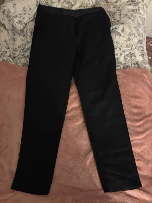 Svarta kostymbyxor från Sandro - Stilrena svarta kostymbyxor från Sandro Paris. Byxorna har rak passform och klassisk midja, perfekta för en clean och modern look. Tillverkade i ett mjukt tyg som ger en snygg siluett. Passar till skjorta eller t-shirt för en trendig outfit. Nypris 3800kr.