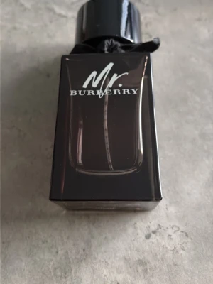 Mr. Burberry parfymflaska - Snygg parfym från Burberry, Mr. Burberry, i en mörk glasflaska med svart lock och en liten svart rosett runt halsen. Flaskan har en stilren och maskulin design som känns lyxig och modern. Perfekt för dig som gillar exklusiva dofter. Säljer en tomflaska frakt 90kr