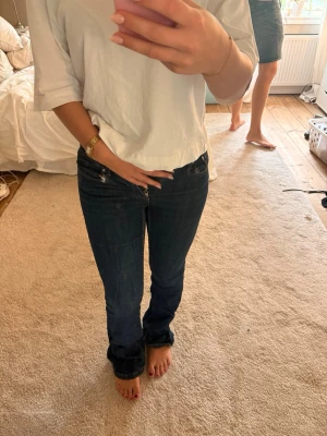 Mörkblå bootcut jeans - Säljer ett par mörkblå bootcut jeans med låg midja och klassiska fem fickor. Jeansen har en enkel design utan slitningar och är tillverkade i ett mjukt denimtyg som sitter snyggt på benen. Perfekta för en avslappnad och trendig look.