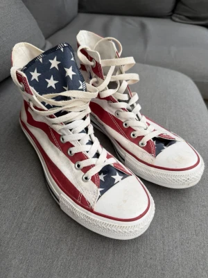 Converse - Säljer ett par höga Converse med amerikanskt flaggmönster. Skorna är storlek 41,5 och har innemåt 26,5 och är i väldigt bra skick! :)