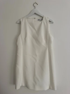 Vit klänning från Zara - Stilren vit klänning från Zara. Klänningen är ärmlös med rund halsringning och har en enkel, rak passform. Tillverkad i ett mjukt material som ger en elegant look. Helt ny med prislapp kvar.