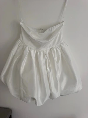 Vit bandeau klänning från Boohoo - Superfin vit kort bandeau klänning från Boohoo med ballongliknande kjol. Klänningen är gjord i ett glansigt polyestertyg som ger en lyxig känsla. Perfekt för dig som vill sticka ut med en unik look. Prislapp kvar. 