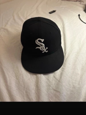 Svart White Sox keps från New Era - Säljer en svart keps från New Era med White Sox-logga broderad i vitt framtill. Klassisk 59FIFTY-modell med rak skärm och broderade ventilationshål. Perfekt för dig som gillar sportig streetstyle och vill ha en ikonisk look.