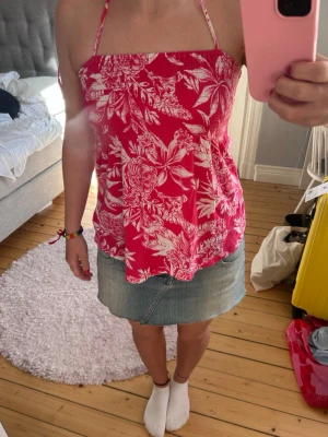 Rosa blommig halterneck linnetopp - Snygg rosa linnetopp med vitt blommigt mönster och halterneck-knäppning. Toppen är ärmlös och resår kring bröstet