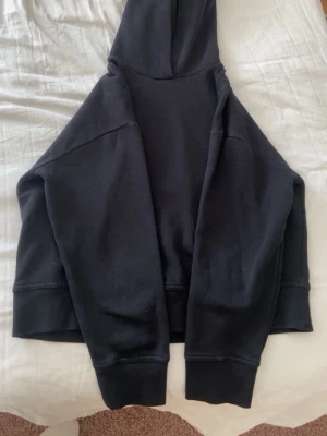 Svart hoodie från Zara - En klassisk svart hoodie från Zara med huva och breda muddar vid ärmslut och nederkant. Tillverkad i mjukt bomullsmaterial som känns skönt mot huden. Perfekt för en avslappnad och stilren look. Den är använd men inget men märker på de sättet.