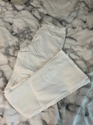 Vita bootcut jeans med medel midja - Säljer ett par vita jeans med bootcut-modell och medel midja. Jeansen har klassisk femficksdesign och stängs med knapp och dragkedja. Materialet är mjukt och stretchigt för skön passform. Perfekta för dig som vill ha en clean och fräsch look.