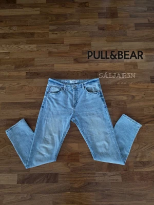 Ljusblå raka jeans från Pull&Bear - 👖 PULL&BEAR Jeans Straight Fit – Storlek 44 (EUR 44 / W34) 👖 Stilrena ljusblå jeans från Pull&Bear med rak straight fit-passform. Klassisk 5-ficksmodell med tidlös design som passar till allt i garderoben. Lätt tvättad denim med snygg fade och bekväm passform. Knappstängning, bälteshällor och originaldetaljer. Mycket fint skick / nyskick utan större slitningar eller skador.  📦 Snabb leverans – skickas samma dag (om ej hindr.) 📩 Kontakta vid frågor