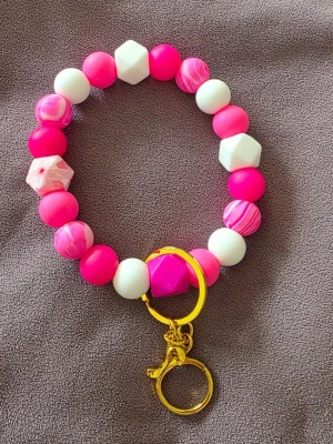 Färgglatt armband med pärlor och nyckelring - Säljer ett handgjort väsksmycke/nyckelring stora pärlor i rosa, vitt och marmorerat mönster. Den har både runda och hexagonformade pärlor samt en guldfärgad nyckelring. Perfekt accessoar för dig som gillar färg och unika detaljer.