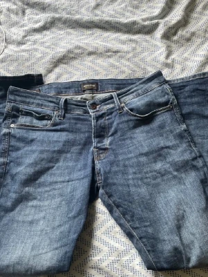 Blå jeans från Jack & Jones - Snygga blå jeans från Jack & Jones med klassisk femficksmodell och diskreta slitningar. Jeansen har normal midja, raka ben och detaljerade sömmar. Perfekta för en avslappnad och trendig stil.