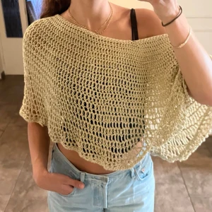 Guldfärgad virkad poncho-topp / nättopp - Superfin handgjord hålmönstrad och virkad topp i en varm beige/guld-nyans med subtilt glitter i garnet. Luftig, draperad modell som kan bäras enkelt off-shoulder eller rak. Kortare croppad längd med snyggt fall och vid silhuett.  Perfekt för festival, sommarkvällar eller över en bikini/ett linne tillsammans med ett par ljusa jeans.  ONESIZE, passa alla i prinicp (har vanligtvis S)