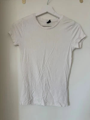 Vit t-shirt från Gina Tricot - En klassisk vit t-shirt från Gina Tricot i mjuk bomull. Modellen är enkel med rund halsringning och korta ärmar, perfekt att matcha med jeans eller kjol. Snygg basic som funkar till allt och är ett måste i garderoben.