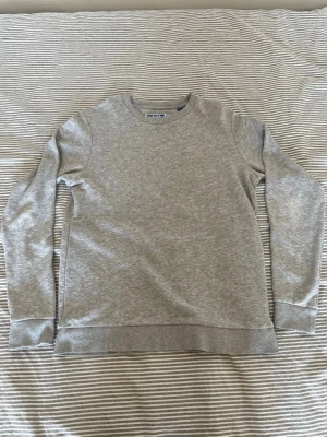 Grå basic sweatshirt - En stilren grå sweatshirt med rund hals och långa ärmar. Tröjan har breda muddar vid ärmslut och nederkant för en klassisk look. Tillverkad i mjukt sweatshirtmaterial som är perfekt för en avslappnad stil.