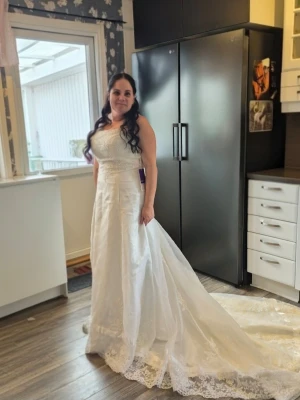 Ivory brudklänning med spetsdetaljer JJ house stl 40 med mån för att göra större - Elegant ivoryfärgad brudklänning från JJ's House med lång släp och vackra spetsdetaljer samt glitter upptill. Klänningen har en axelbandslös design och är tillverkad i ett glansigt material med broderade mönster på överdelen och även kjolen. De är även glitter längst ned på klänningen. Otroligt vacker klänning som köptes som en plan b ifall min drömklänning inte skulle hinna komma hem. Endast provad. Tags kvar.. Stl 40 men går att snöra lite större o lite mindre. 