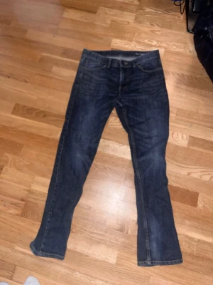 Mörkblå Hank regular fit jeans - Säljer ett par mörkblå Hank jeans i regular fit med klassisk femficksdesign. Jeansen har raka ben och är tillverkade i slitstarkt denimtyg. Perfekta för dig som gillar en tidlös och enkel stil. 