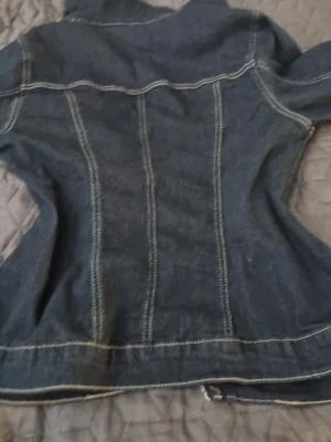 Mörkblå figursydd jeansjacka - Snygg mörkblå jeansjacka med markerade vita sömmar och figursydd passform. Klassisk krage och långa ärmar. Perfekt för dig som vill ha en tidlös och trendig jacka i garderoben. I väldigt fin skick storlek M