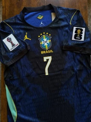 Brasilien matchtröja Vini Jr Nr7 - Säljer en officiell Brasilien matchtröja i svart och blått med gula detaljer och nummer 7 på bröstet. Den kommer ny med prislapp, fraktar inom 0-1 dagar.