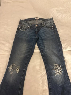 Gina jeans tall - Säljer ett par blå jeans med slitningar och stora hål på båda benen. Jeansen har klassisk femficksmodell och knappgylf. Perfekta för dig som gillar en avslappnad och trendig stil. Från Gina 14+☺️☺️