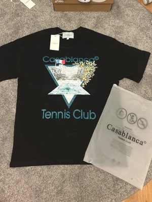 Casablanca Tennis Club svart t-shirt - Casablanca Tennis Club t-shirt i svart med stort grafiskt tryck framtill i blått, vitt och gult. Klassisk rund hals och korta ärmar. Den är riktigt unik och fet, fraktar inom 0-1 dagar📦