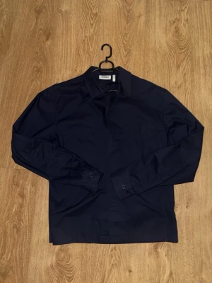 Mörkblå overshirt från Weekday - Stilren mörkblå overshirt från Weekday med klassisk krage och två bröstfickor. Perfekt att bära öppen eller stängd för en clean look. Ny, storlek XS passar S